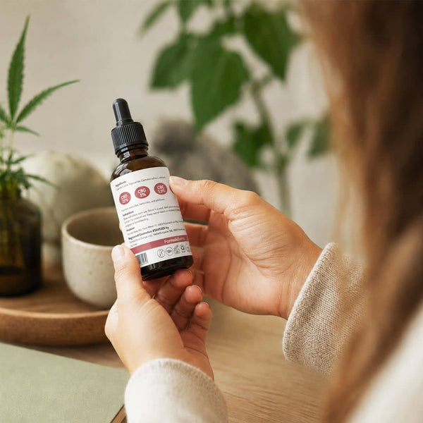 Donna che esamina l'etichetta su una bottiglia di olio di cannabinoidi Formula Swiss in un ambiente interno luminoso.